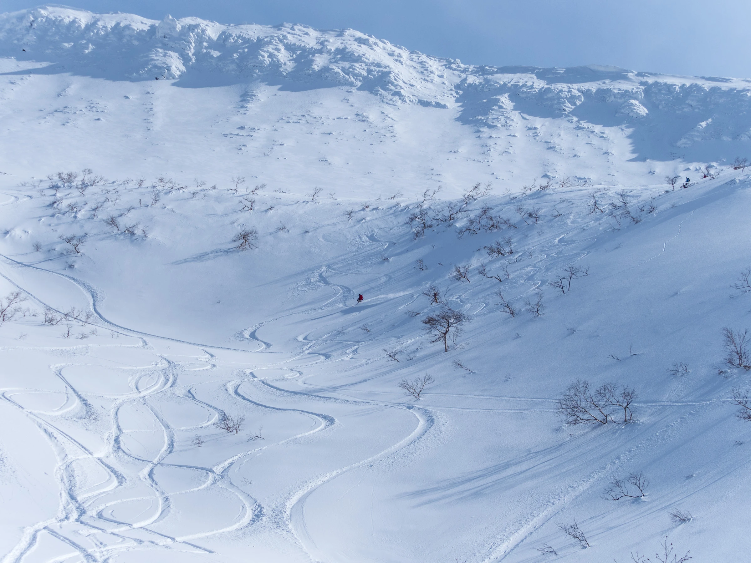 An immense snow-covered cirque and a small red-clad skier in Kaun Bowl, Hokkaido.